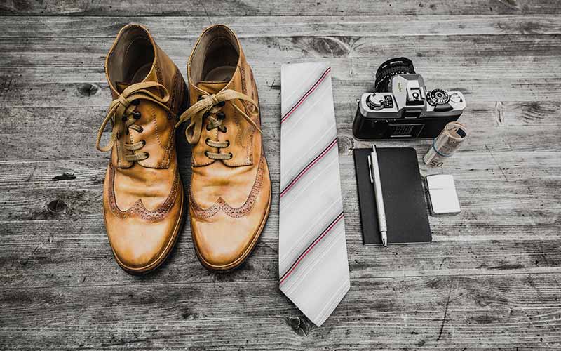 A pair of shoes, tie and camera on the ground.