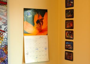 A wall with several pictures and a calendar.
